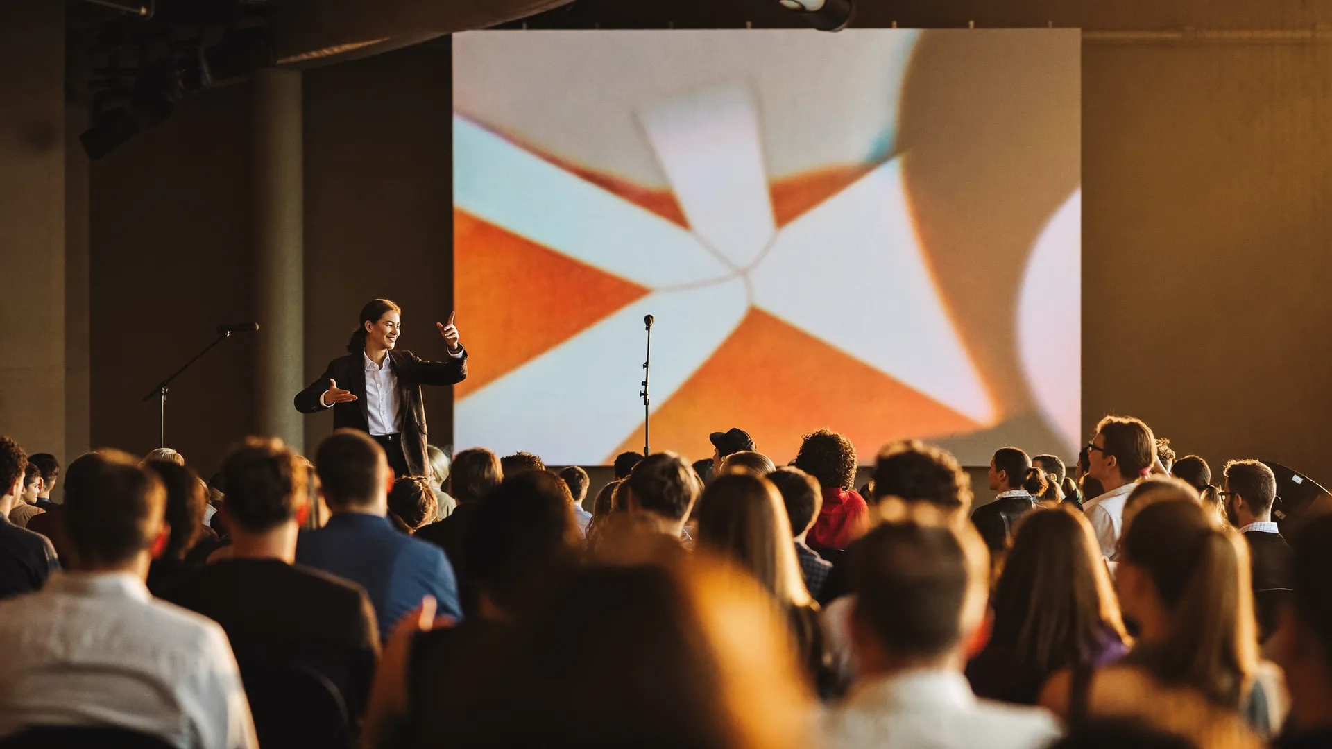 Palestrante num palco de keynote diante da plateia, com telão em tons quentes