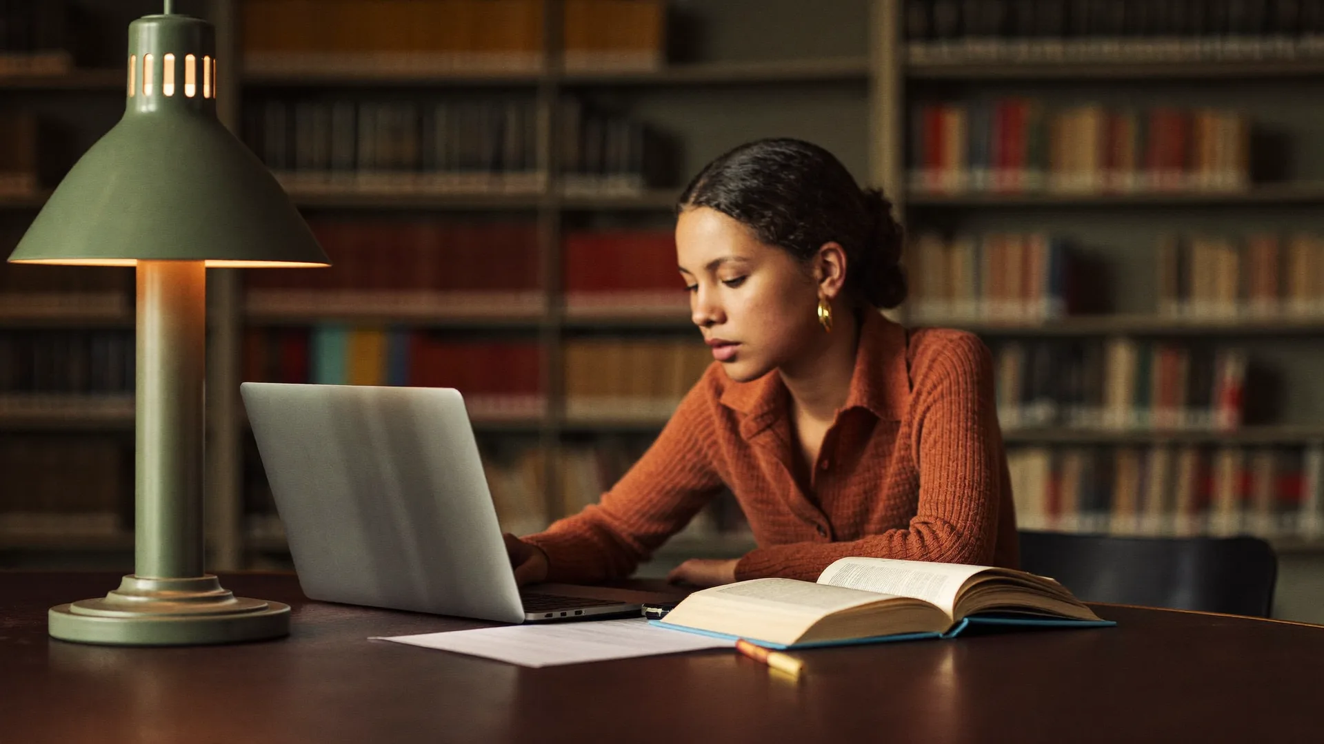 Estudante concentrada com notebook e livro numa biblioteca